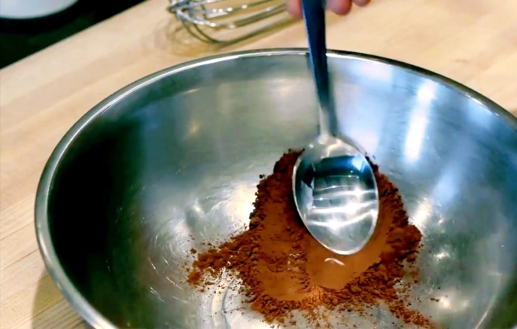 A spoon smooths over chocolate powder in a bowl